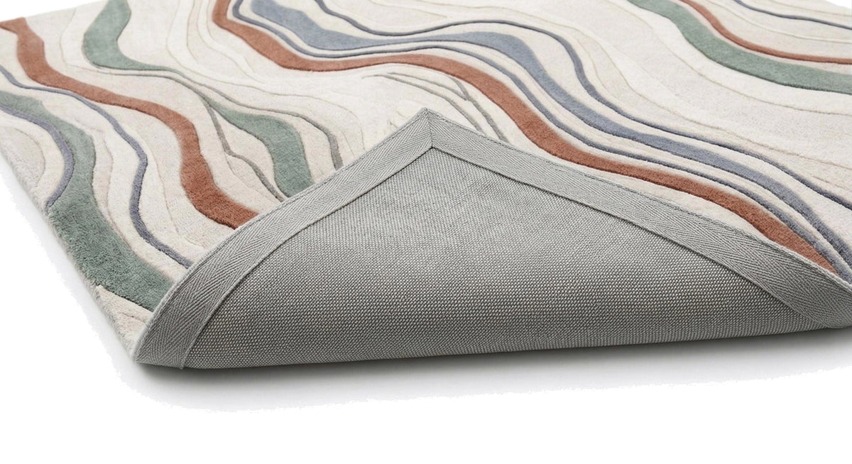 Le coin replié du tapis en laine ivoire et terracotta dévoile son envers tissé gris et son relief sculpté