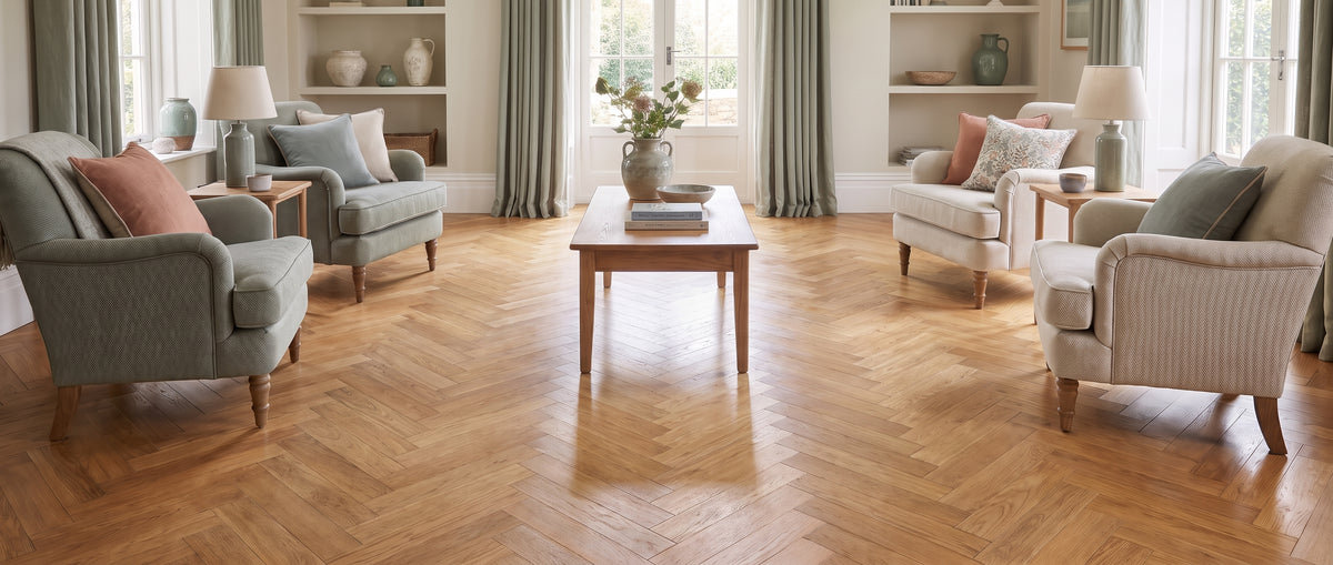 Pièce élégante sans tapis : un parquet en bois clair à chevrons brille au sol entre des fauteuils confortables