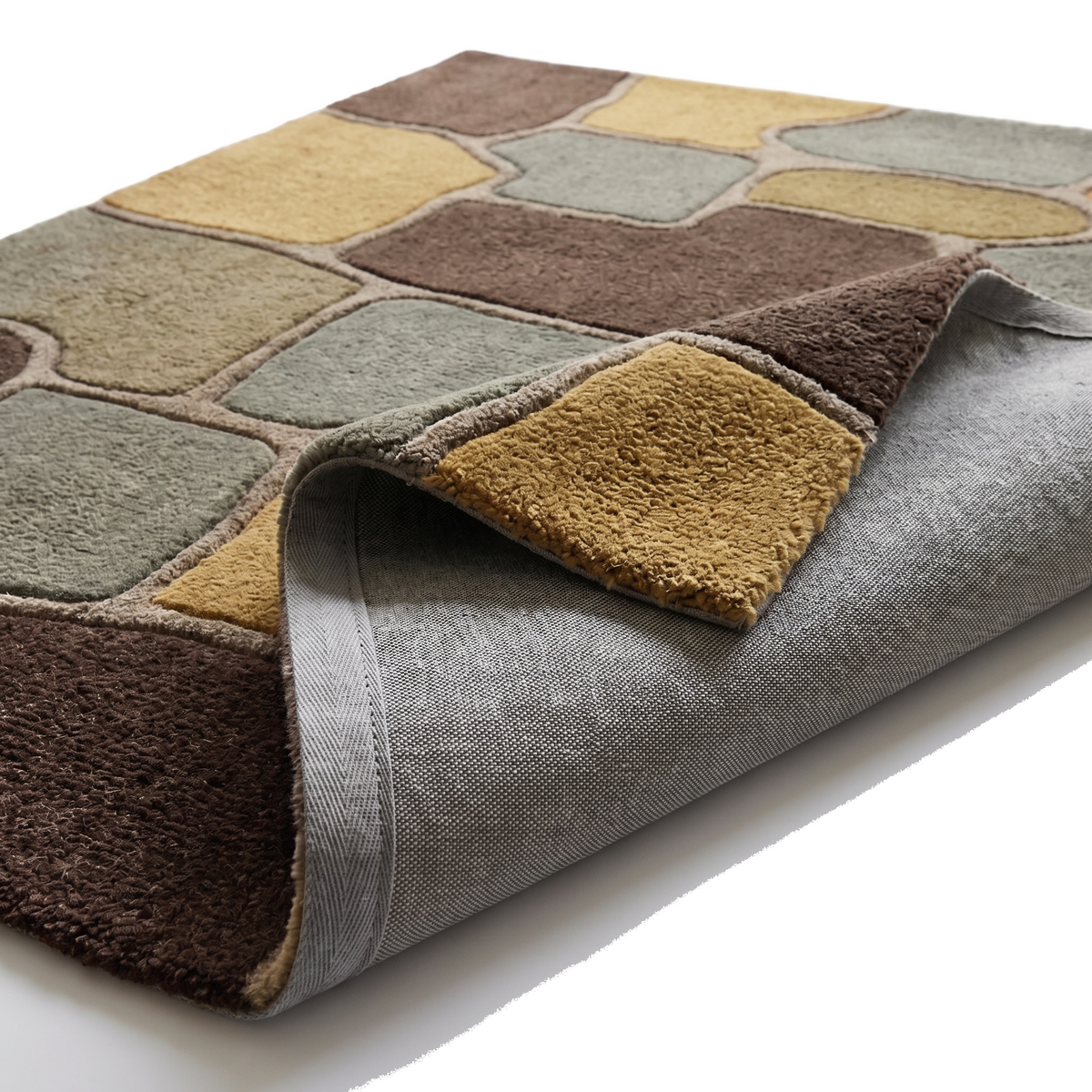 Le tapis plié dévoile sa laine sculptée ocre, marron et vert sauge, son épaisseur moelleuse et son envers tissé