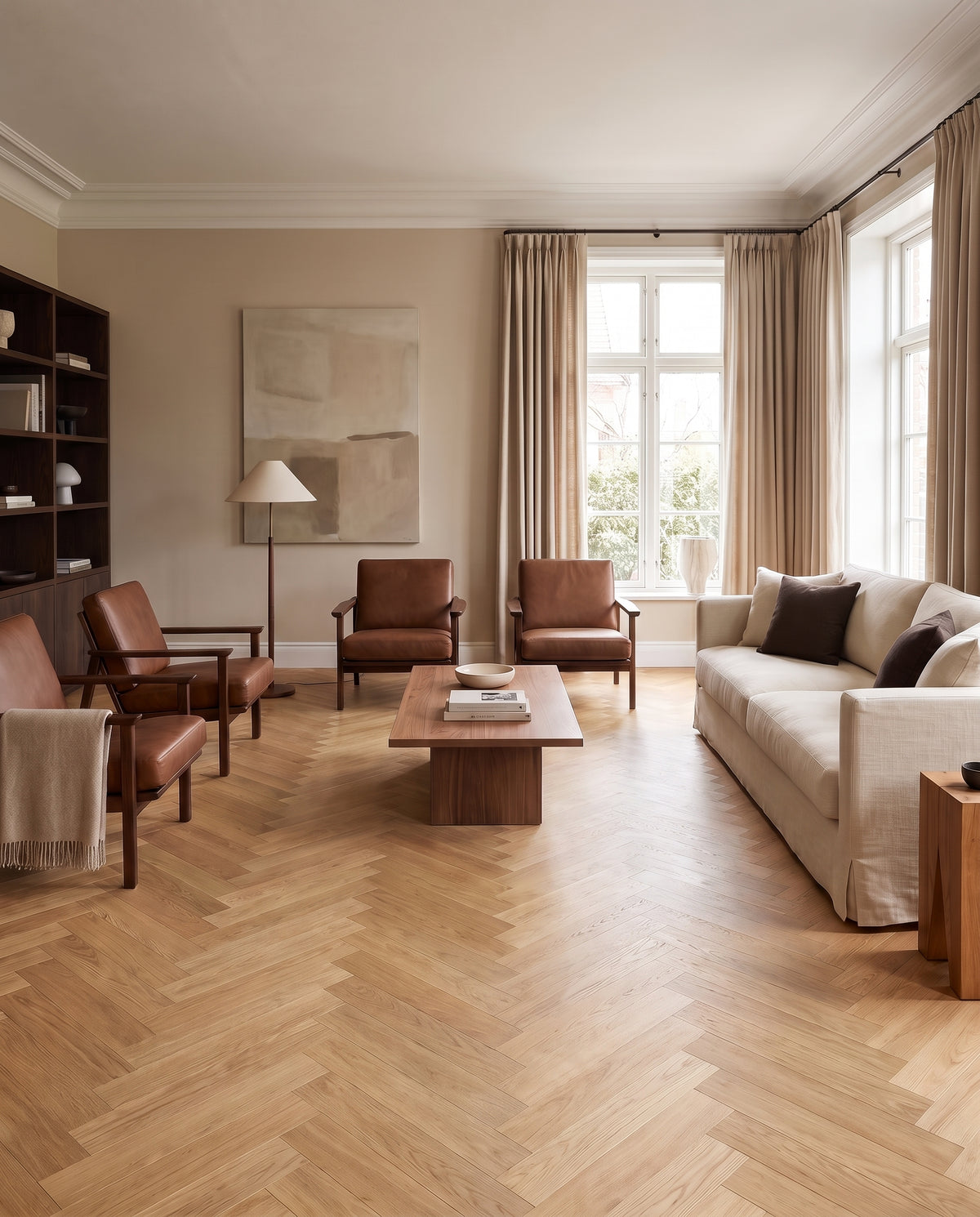 Pièce sans tapis, un salon au sol parqueté en chevrons clairs, avec canapé crème, fauteuils cuir et table basse en bois