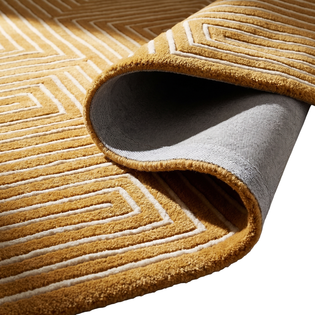 L'envers gris et l'épaisseur d'un tapis ocre en laine tuftée main, au motif labyrinthique ivoire en relief