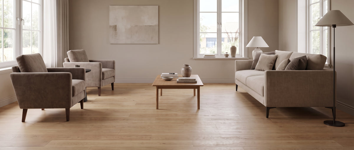 Un salon clair au parquet de bois nu, avec deux fauteuils taupe et un canapé beige autour d'une table basse en bois