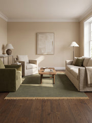 Son tissage main strié donne à ce tapis rectangulaire vert olive en laine un bord beige et des franges, dans un salon