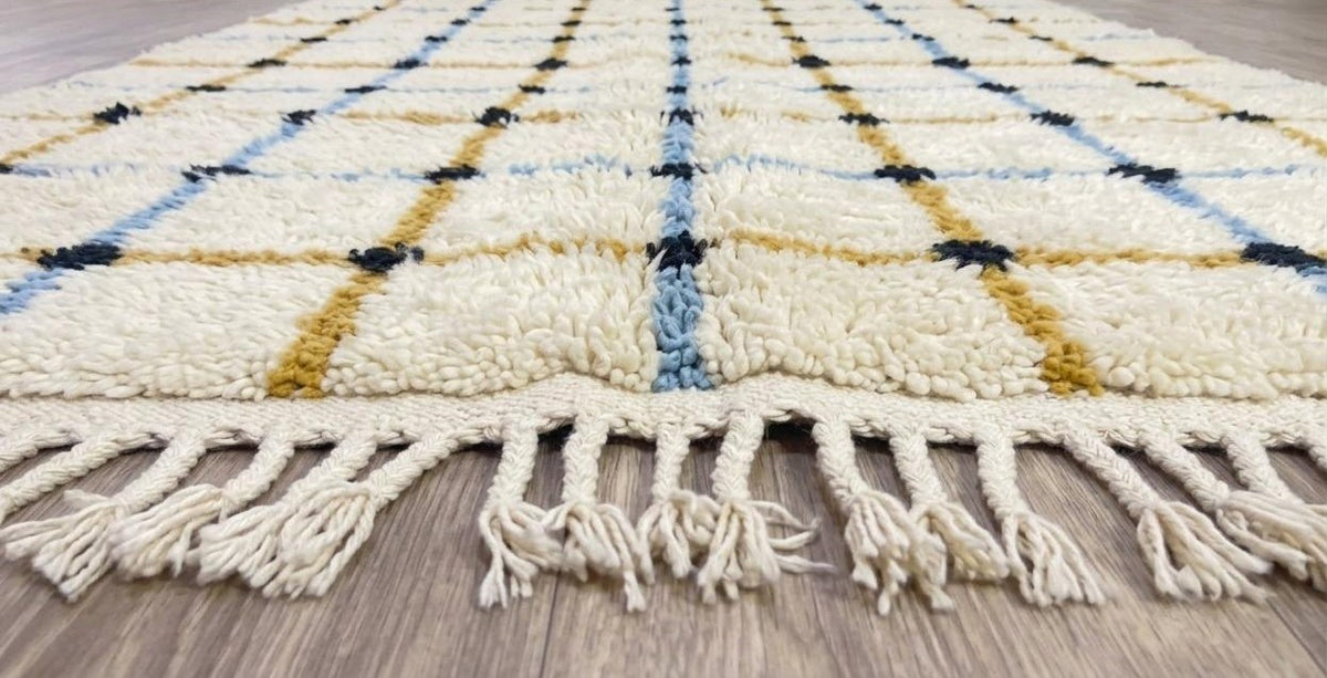 Tapis berbère à carreaux blanc et moutarde Tafrin posé au sol vu de côté, noué main au Maroc