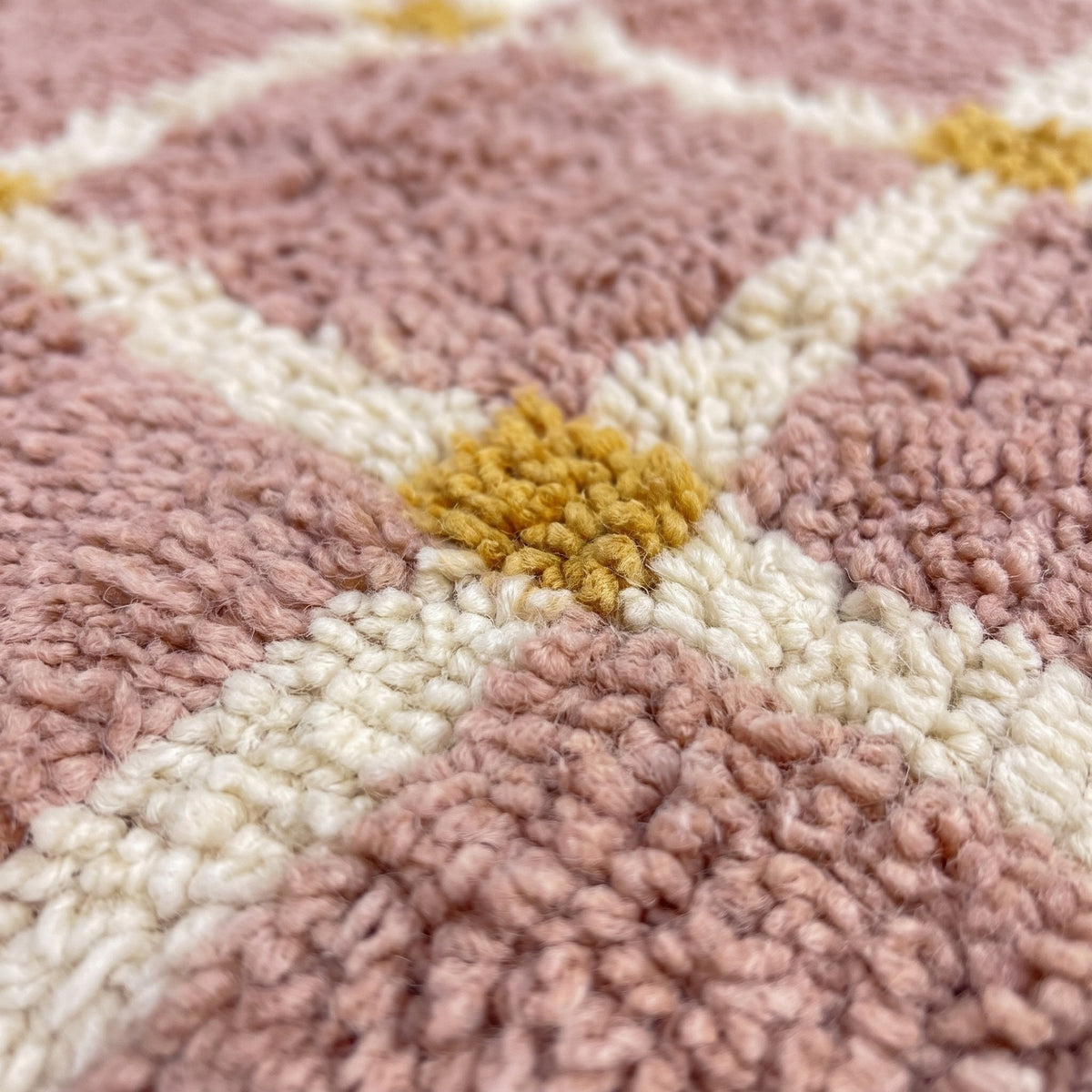 Gros plan sur un motif du tapis berbère Tizwira, fond rose poudré, quadrillage régulier de fines lignes