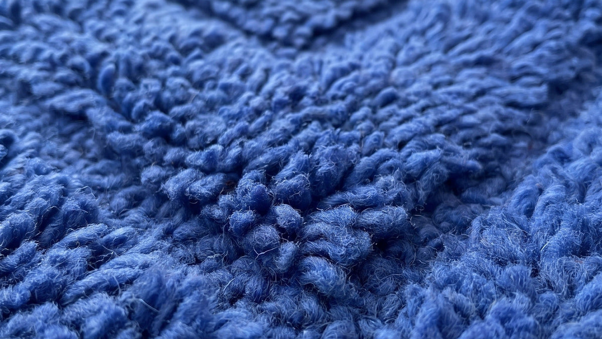Gros plan sur la laine du tapis berbère Tirelwa, poil bleu noué à la main