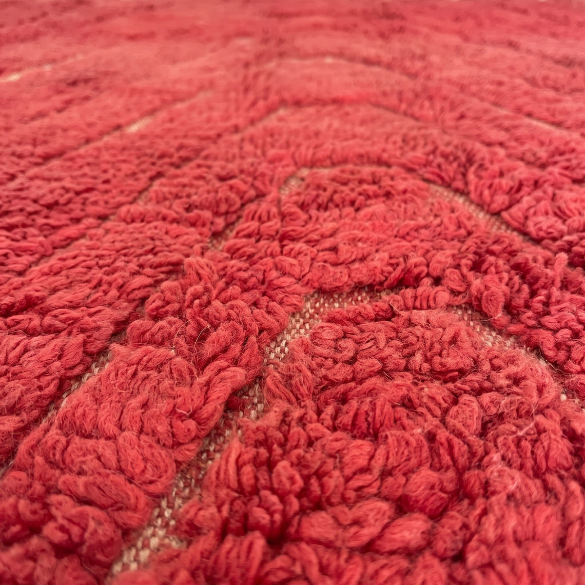 Gros plan sur un motif du tapis berbère Midrane, rouge coquelicot uni à poil long épais