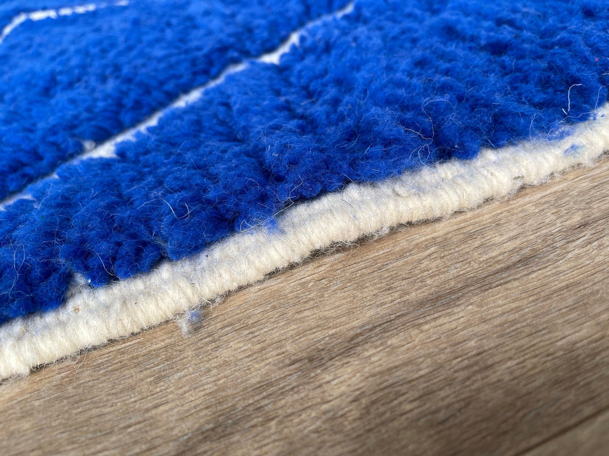 Gros plan sur le coin relevé du tapis berbère Asigna, épaisseur du poil long et dos tissé à la main