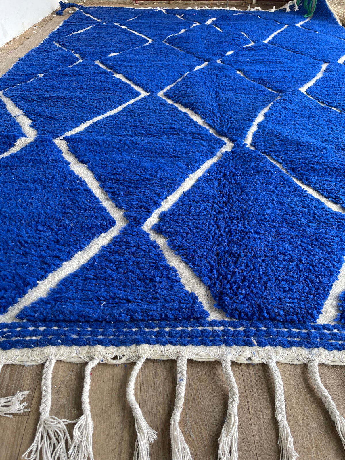 Gros plan sur les franges du tapis berbère Asigna, écrues tressées, nouées à la main