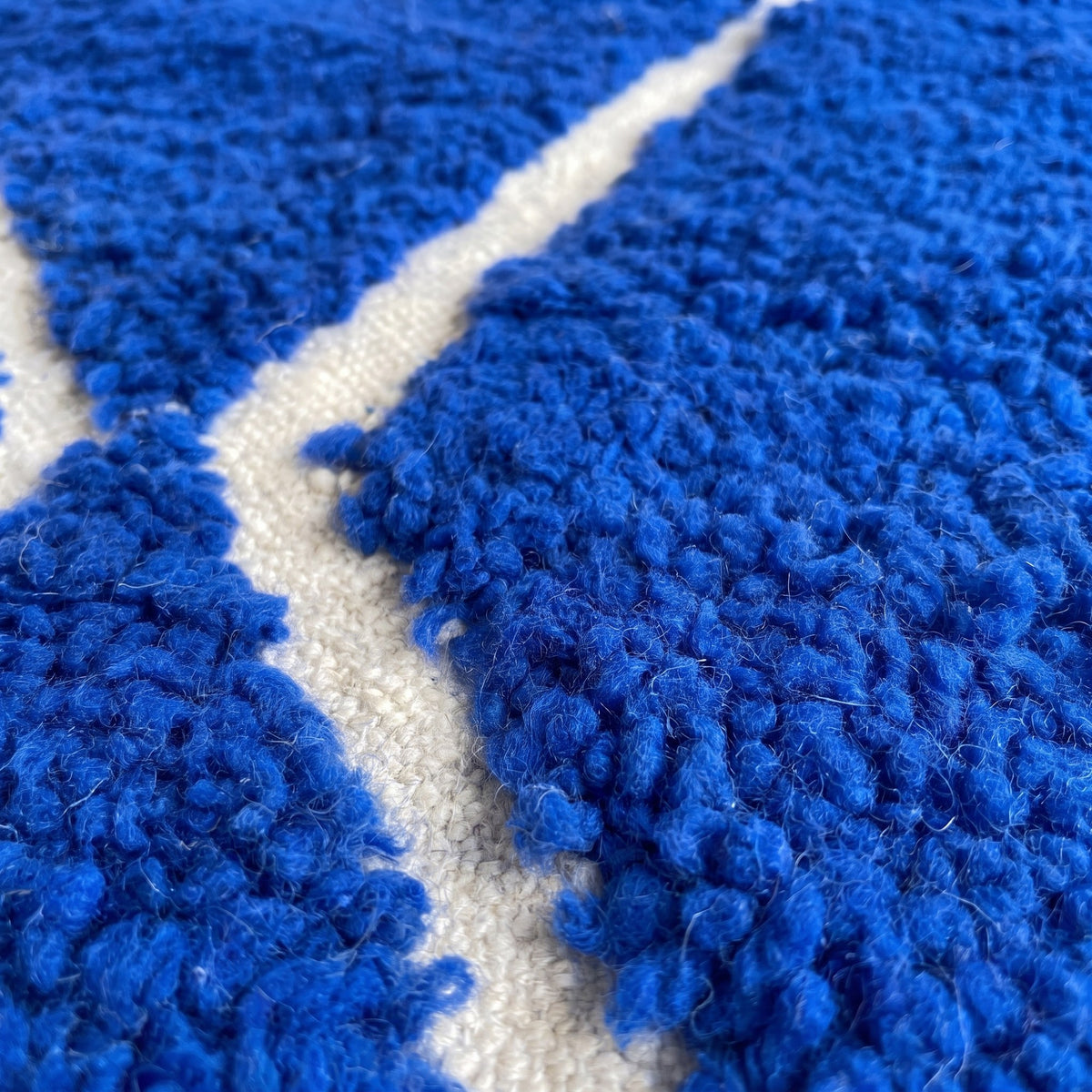 Gros plan sur un motif du tapis berbère Asigna, fond bleu roi uni, treillis de fines lignes