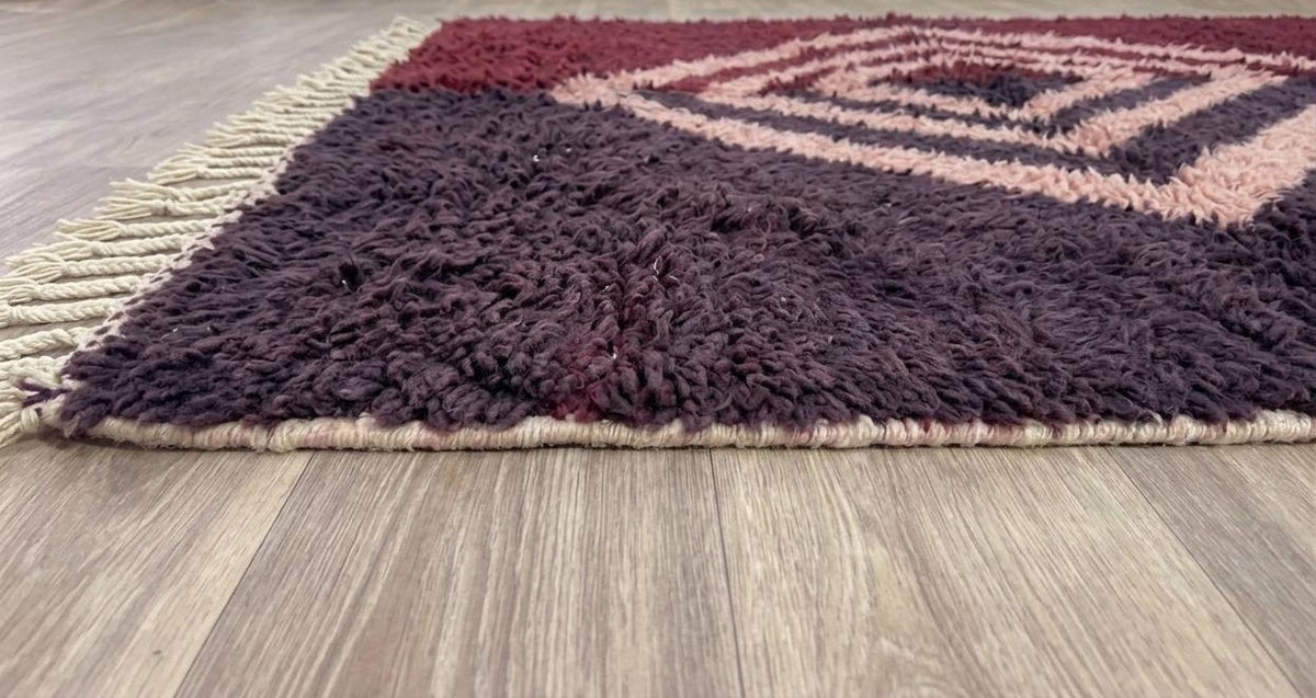 Tapis berbère à losanges bordeaux et rose Ulawen posé au sol vu de côté, noué main au Maroc