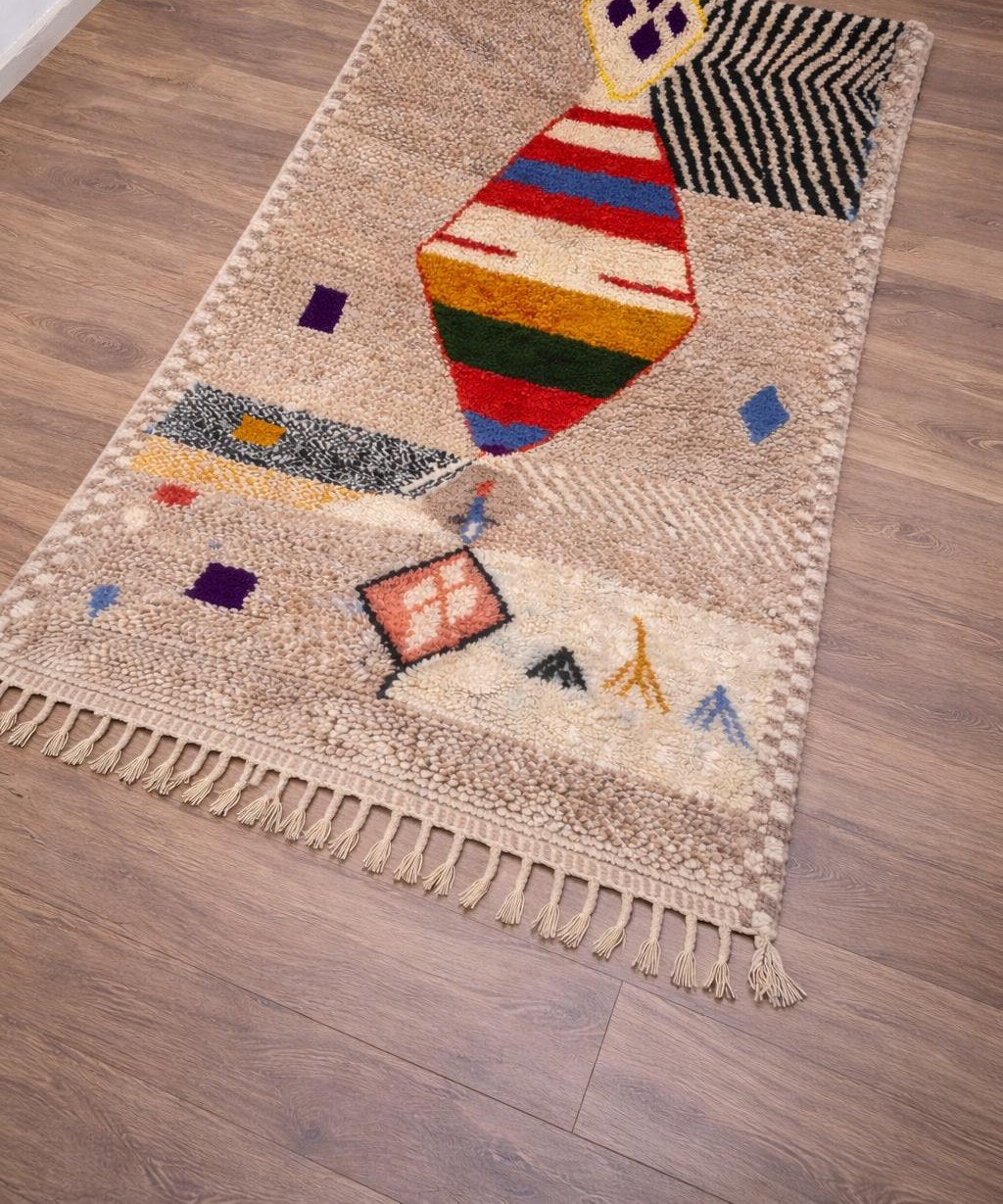Tapis berbère à motifs beige sable Ahaggar posé au sol vu de côté, noué main au Maroc