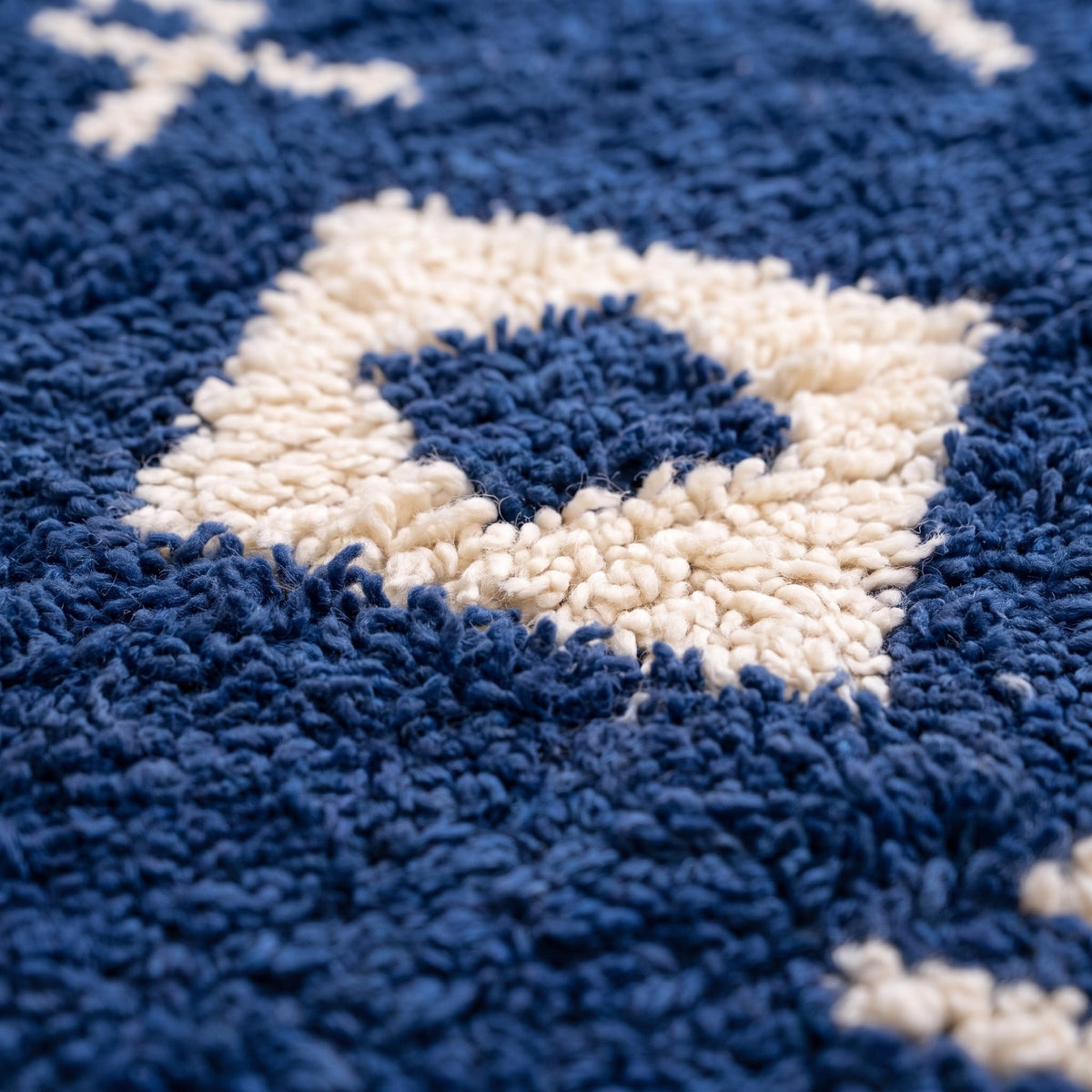 Gros plan sur un motif du tapis berbère Ansegmir, fond bleu marine poil long, symboles écrus