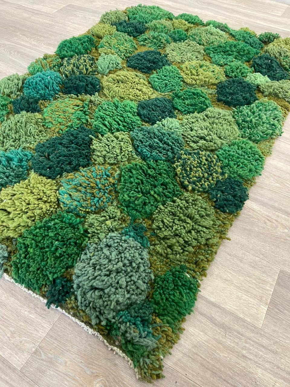 Tapis berbère à motifs vert mousse Zinat posé au sol vu de côté, noué main au Maroc