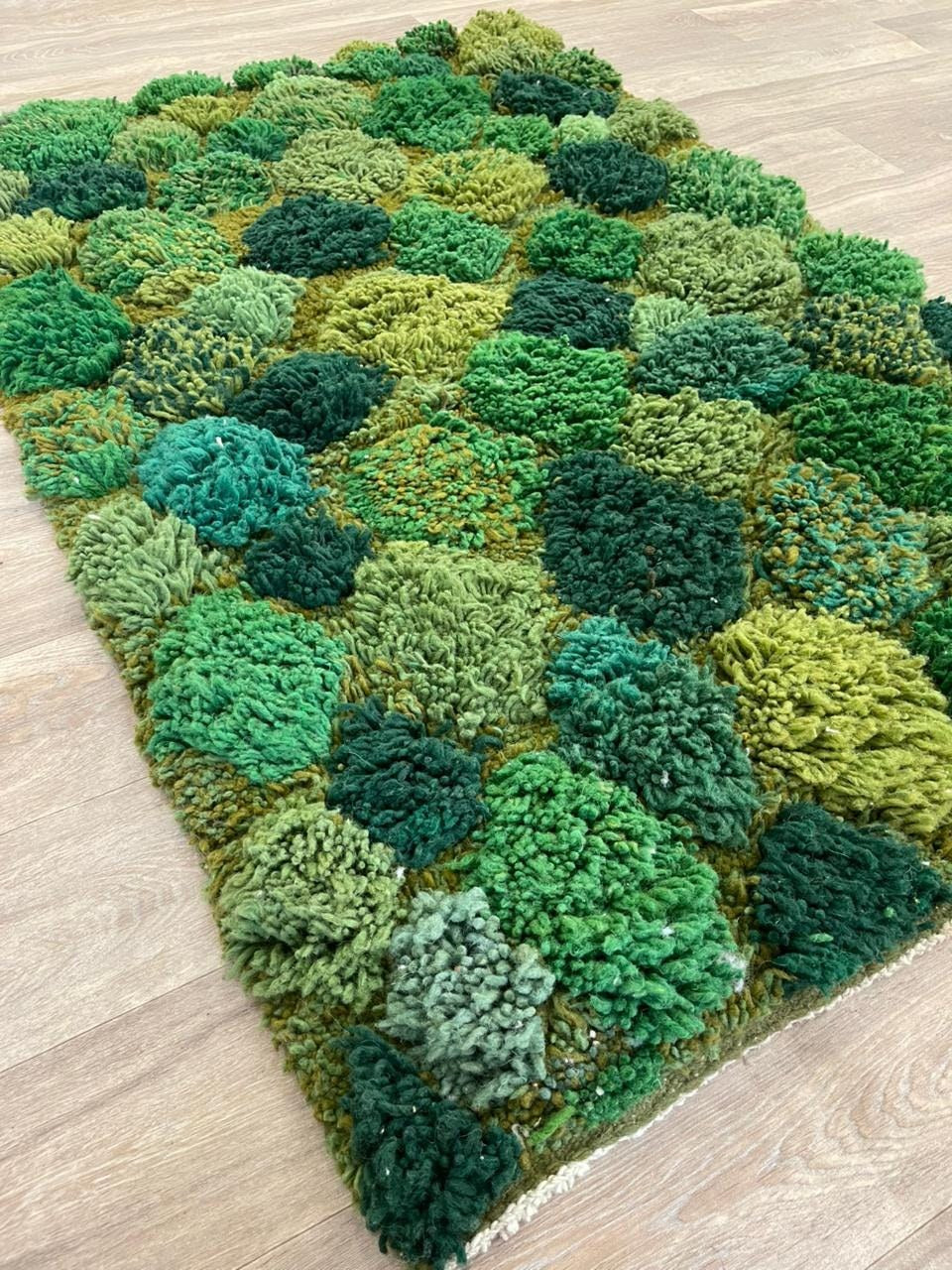 Tapis berbère à motifs vert mousse Zinat posé au sol vu en biais, noué main au Maroc