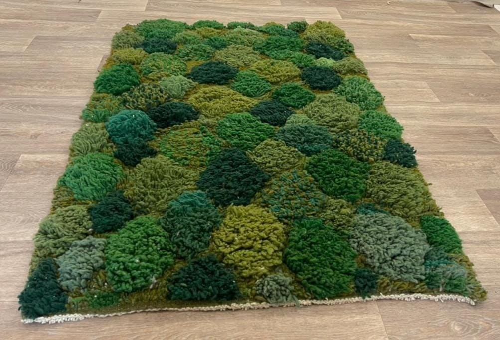 Tapis berbère à motifs vert mousse Zinat posé au sol vu de trois quarts, noué main au Maroc