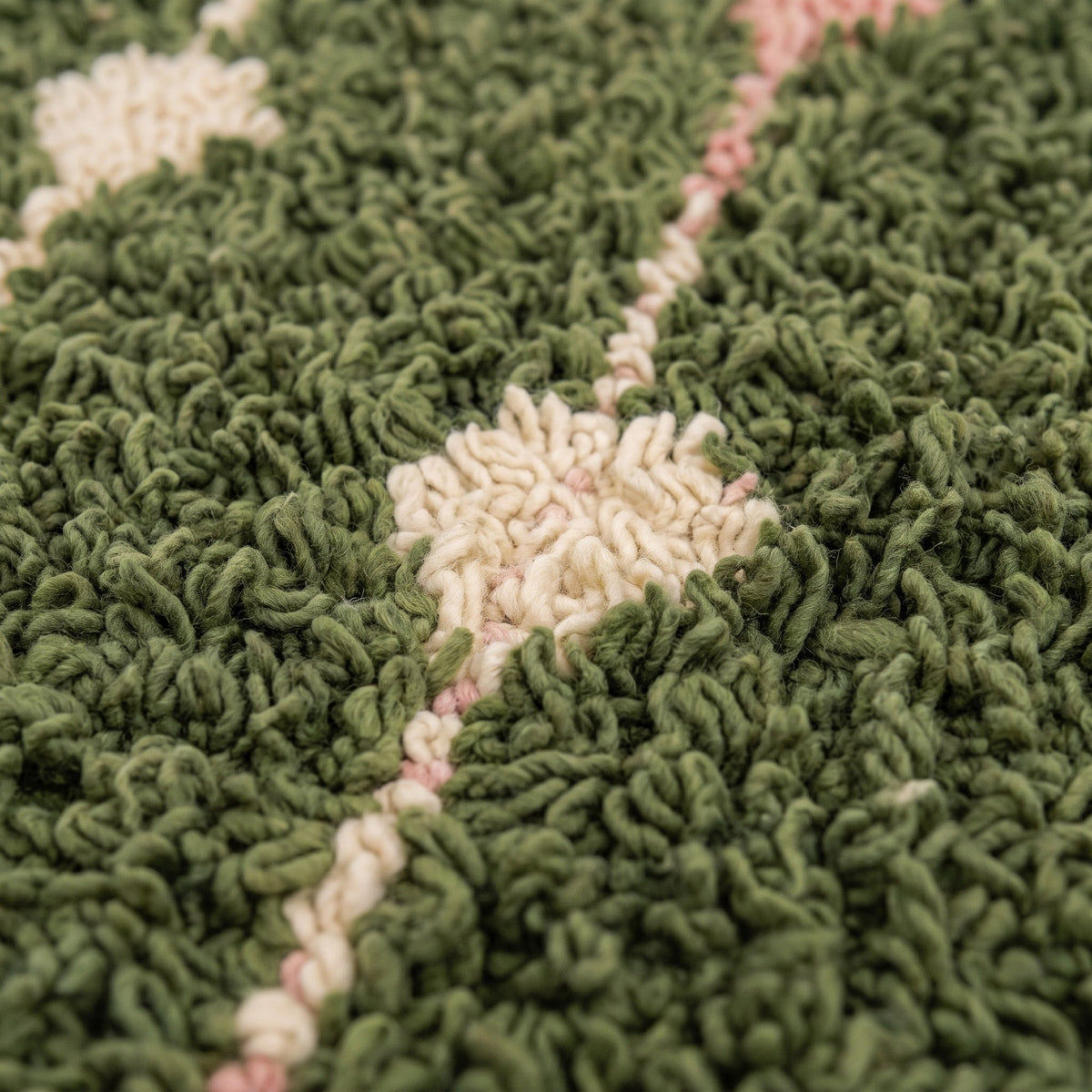 Gros plan sur un motif du tapis berbère Elmoura, fond vert olive à poil long