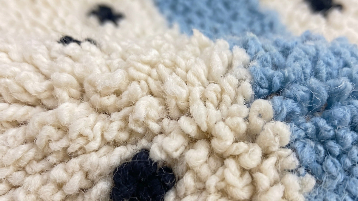 Gros plan sur la laine du tapis berbère Tadmil, poil blanc et bleu ciel