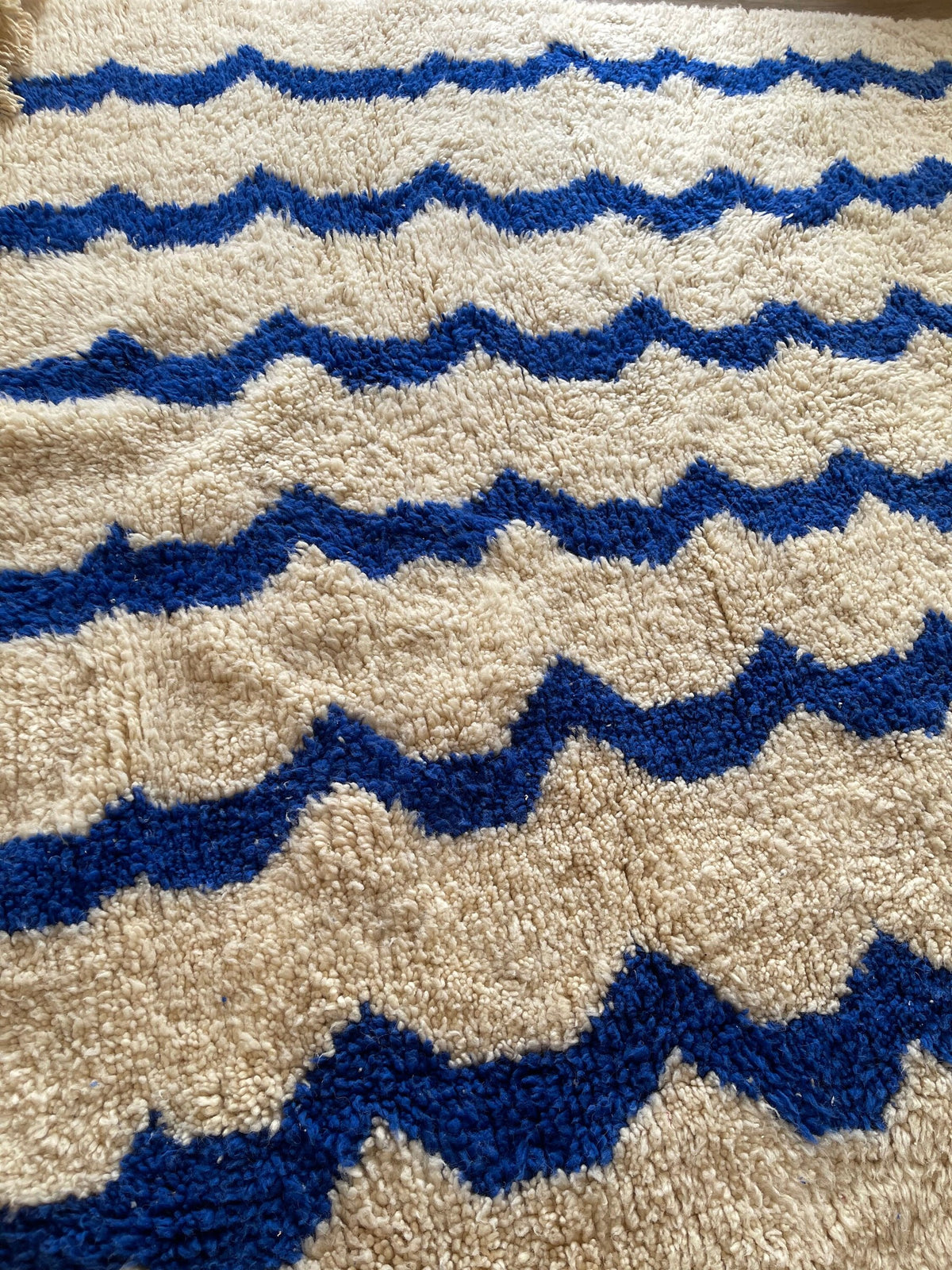 Gros plan sur les franges du tapis berbère Tigrigra, écrues tressées à pompons, nouées à la main