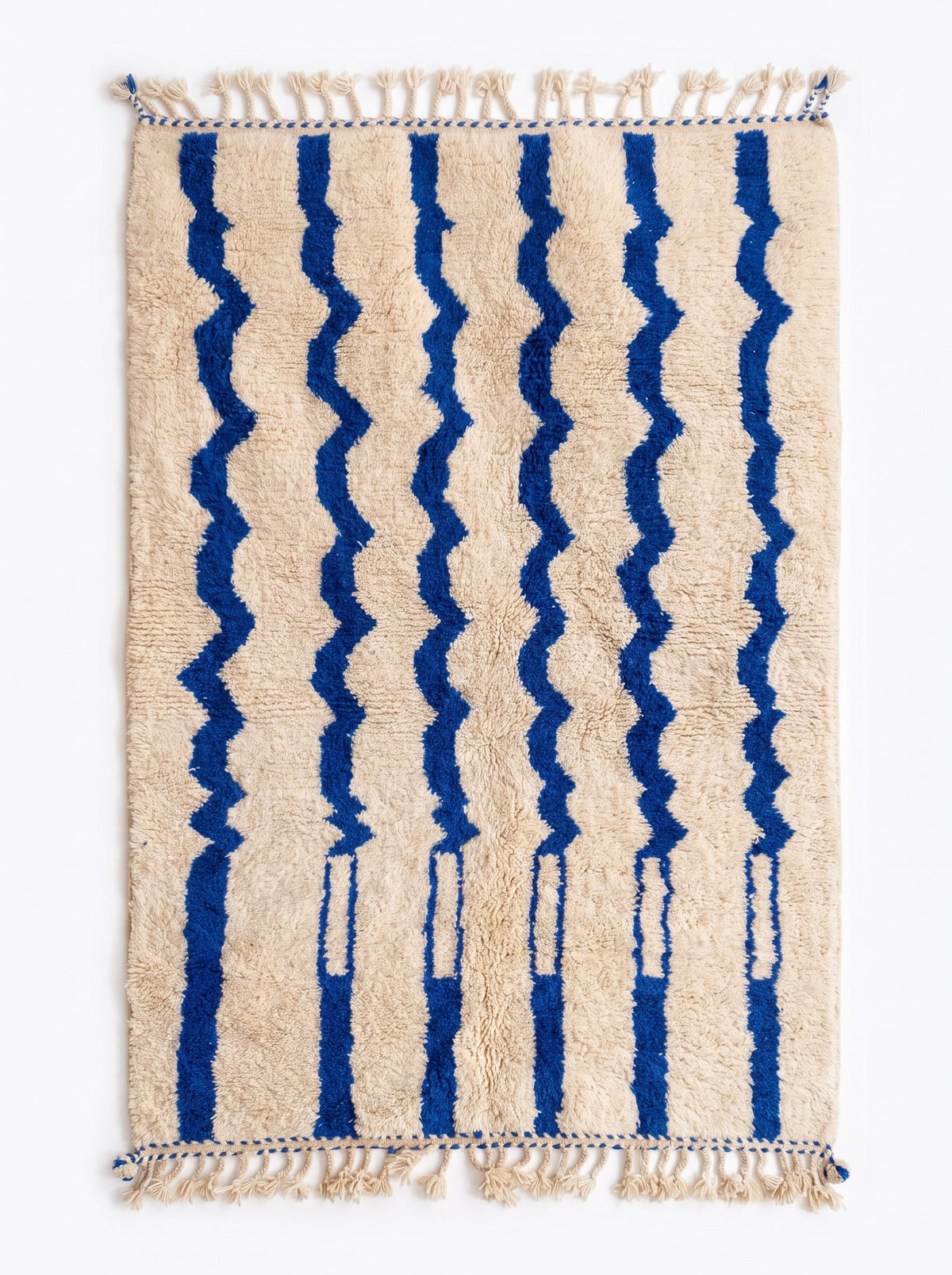 Tapis berbère à rayures blanc et bleu Tigrigra vu à plat, fond écru chaud à poil long parcouru, franges écrues tressées à pompons