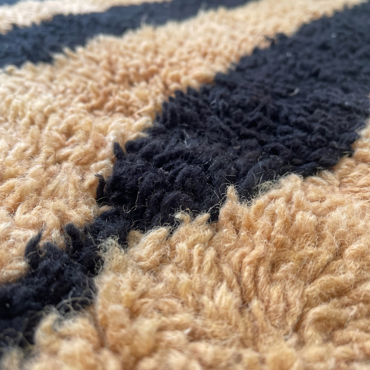 Gros plan sur un motif du tapis berbère Tazroun, champ à poil long, fond camel