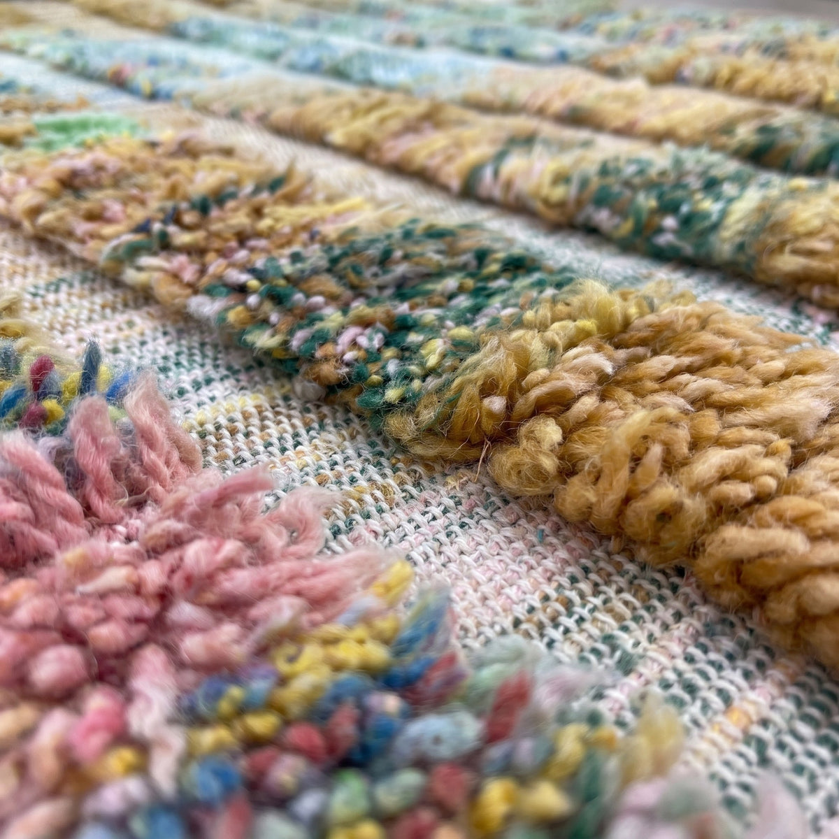 Gros plan sur un motif du tapis berbère Tissa, base tissée plate claire chinée, bandes verticales
