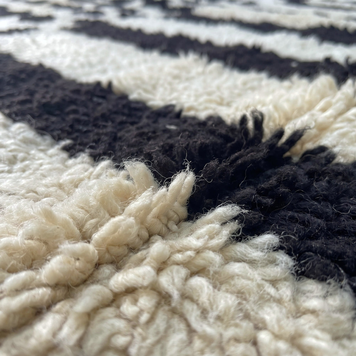 Gros plan sur un motif du tapis berbère Igherm, fond ivoire à neuf rayures verticales noires irrégulières