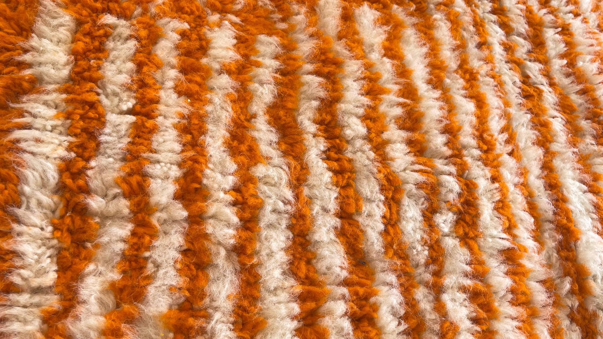 Gros plan sur la laine du tapis berbère Iknioun, poil orange noué à la main