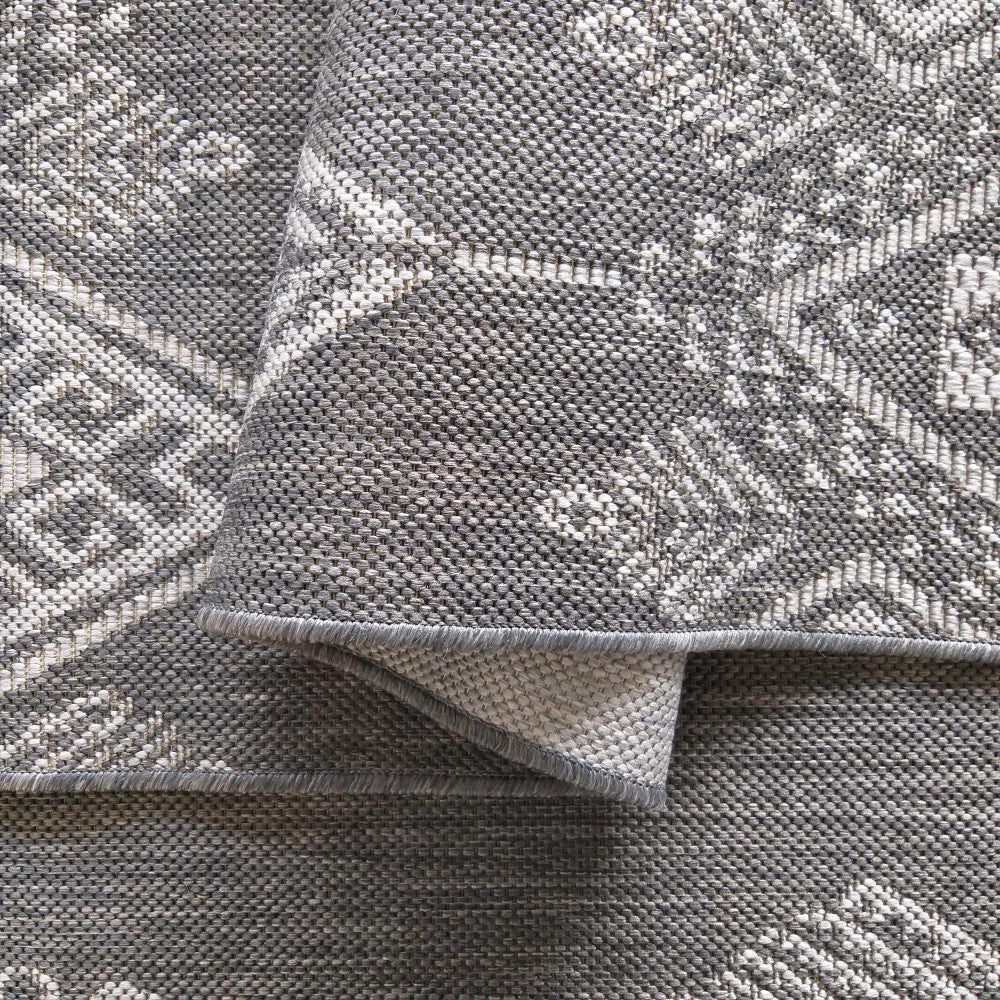 Tapis tissé gris et blanc avec motifs géométriques complexes. Une partie du tapis est repliée, montrant son envers
