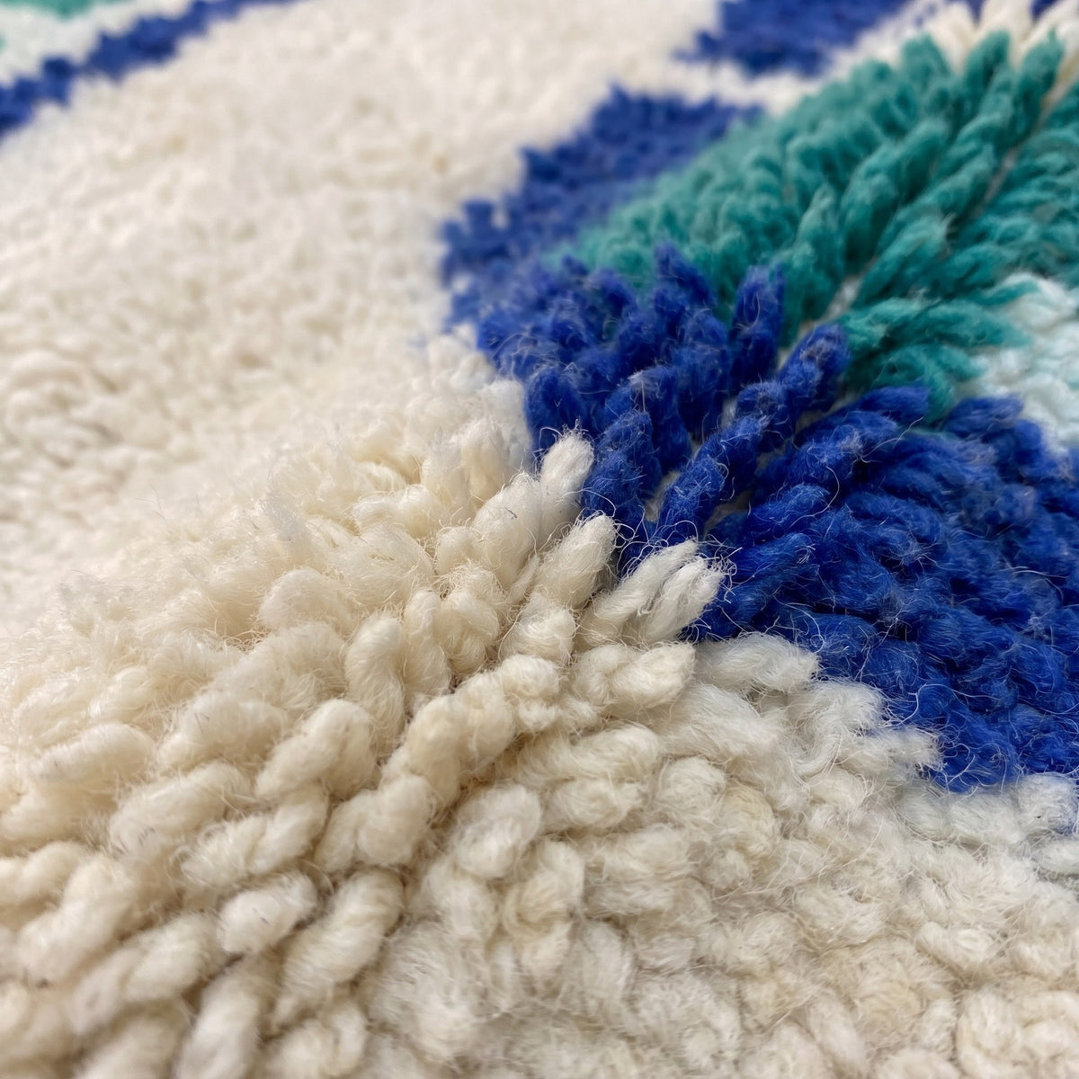 Gros plan sur un motif du tapis berbère Mezgal, fond blanc, à gauche douze barrettes bleues