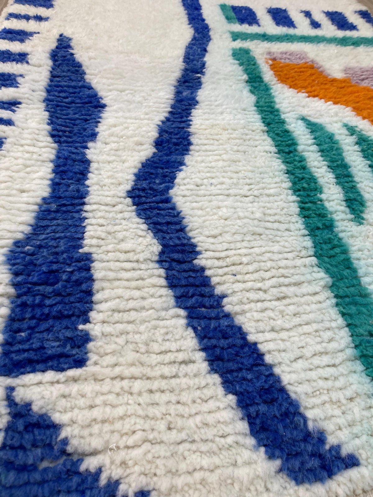 Gros plan sur la laine du tapis berbère Mezgal, poil blanc et bleu noué à la main
