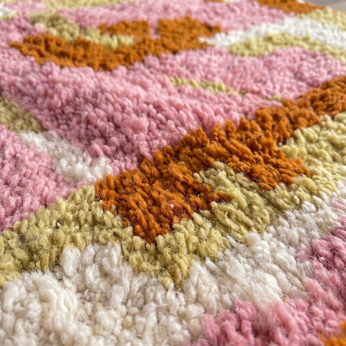 Gros plan sur un motif du tapis berbère Skoura, cadre rouille sur les côtés, fond rose poudré