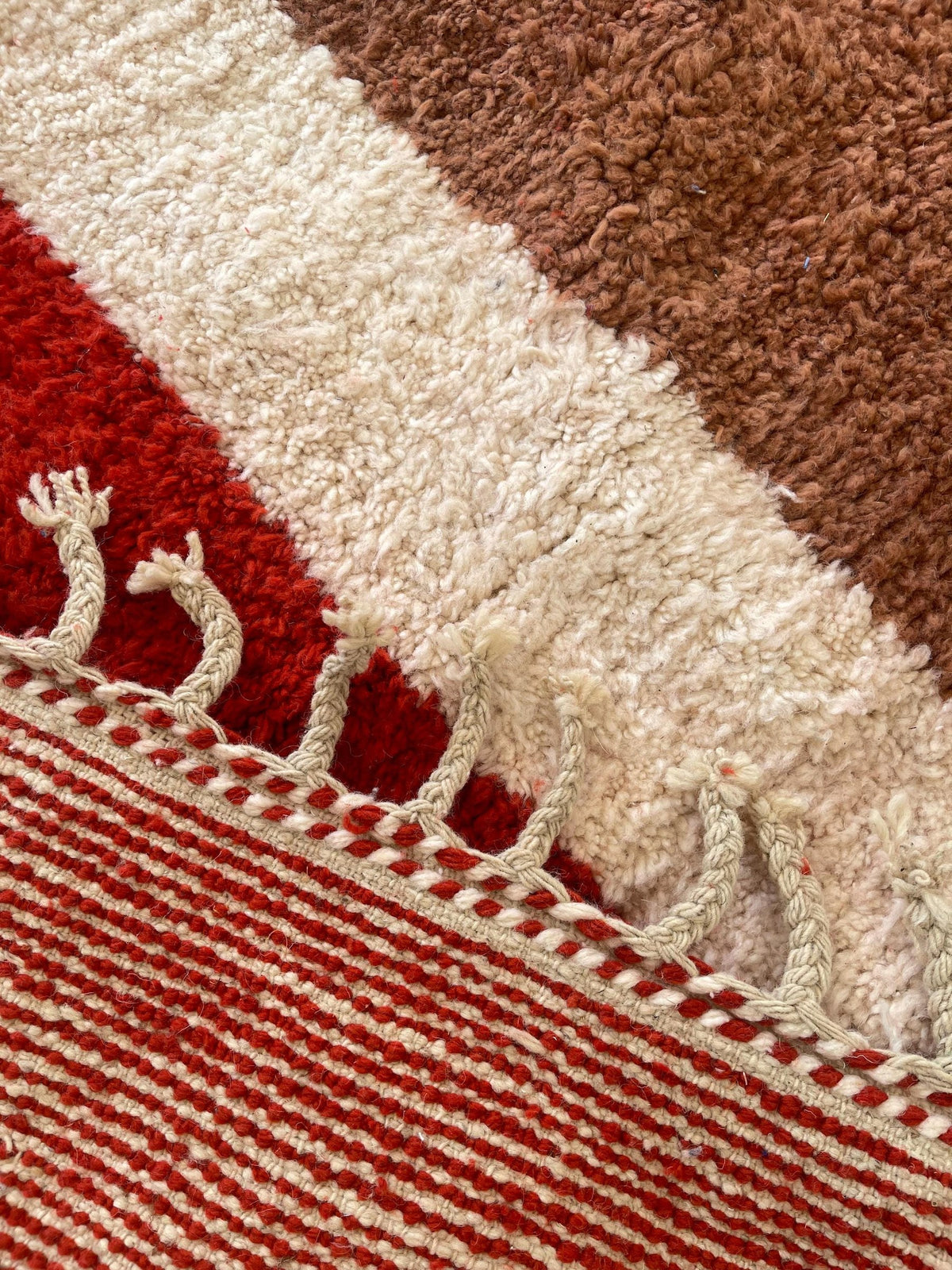 Gros plan sur les franges du tapis berbère Boudnib, écrues à liseré rouge, nouées à la main