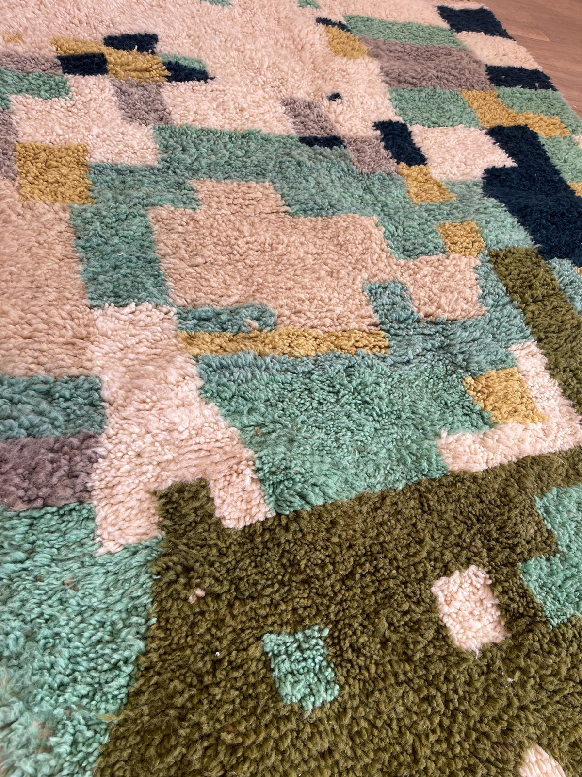 Gros plan sur un détail du tapis berbère Tessaout, poil long et motif vert et blanc vus de près