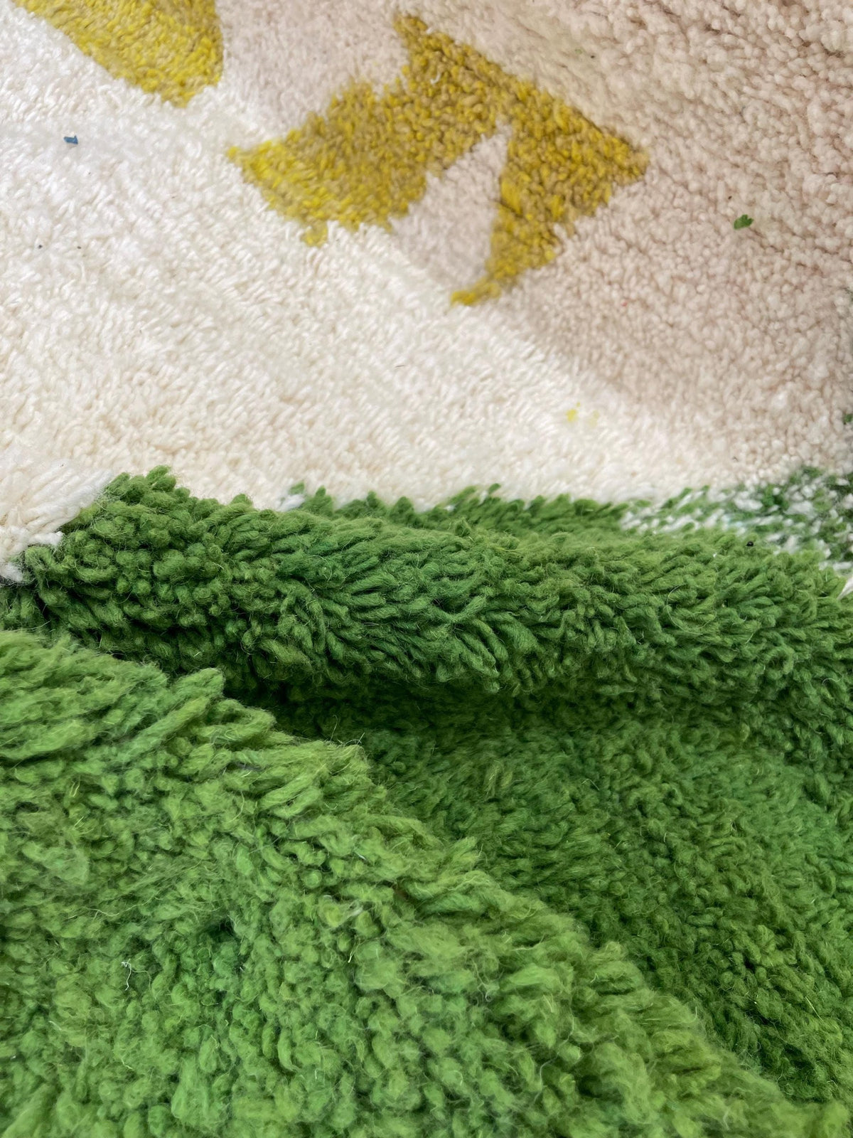 Gros plan sur la laine du tapis berbère Tounfite, laine de mouton au poil long, verte et moutarde