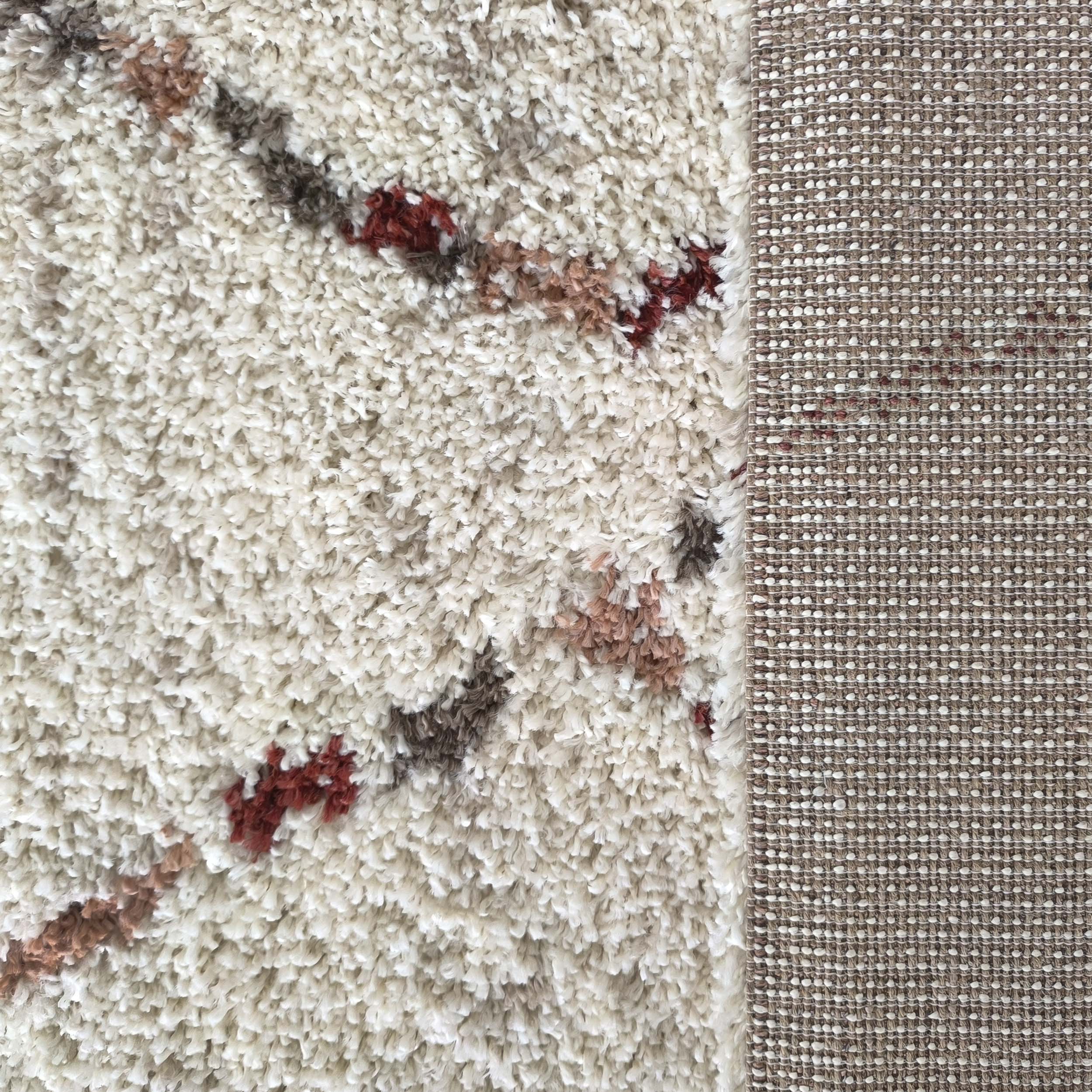 Tapis à poils longs crème avec des motifs abstraits brun et terre cuite, son envers tissé beige à pois blancs est visible sur la droite