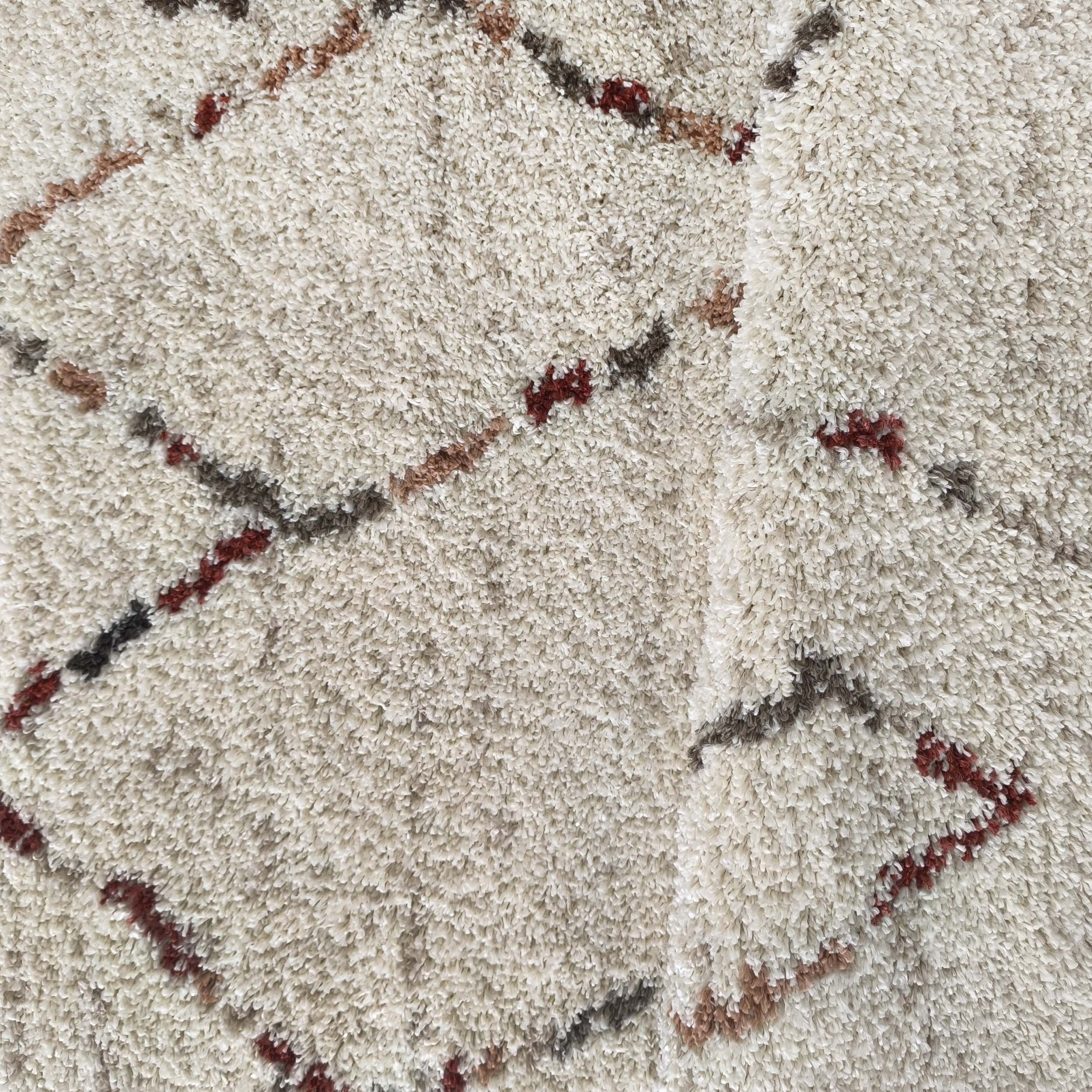 Tapis à poils longs crème avec des motifs de lignes obliques irrégulières et de losanges en marron, gris foncé et bordeaux