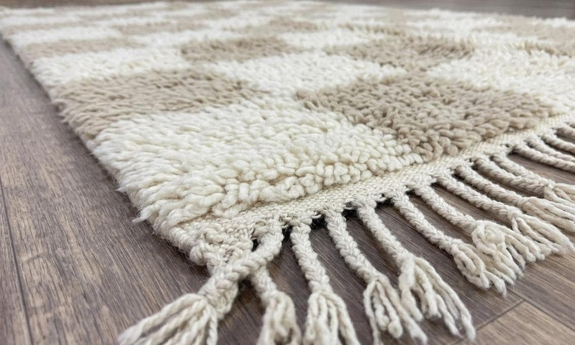 Tapis berbère damier beige et blanc Borzan posé au sol vu de côté, noué main au Maroc