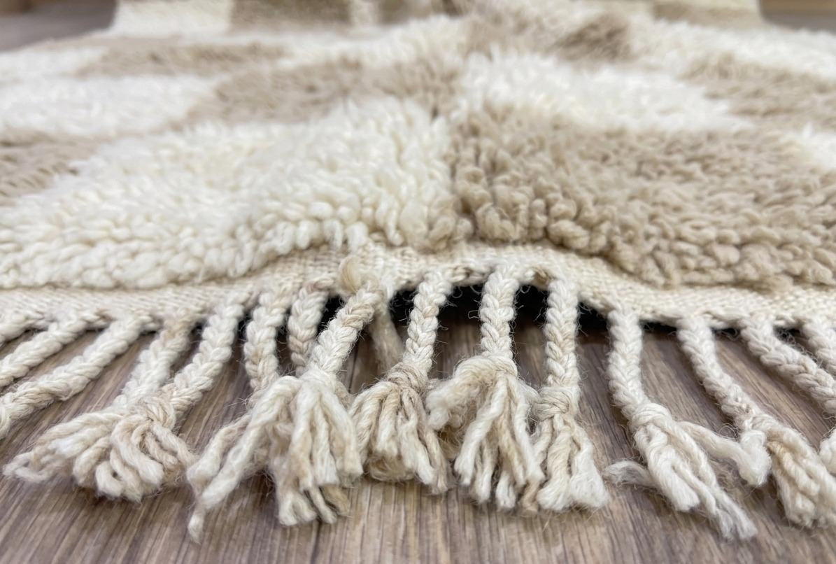 Gros plan sur les franges du tapis berbère Borzan, écrues tressées, nouées à la main
