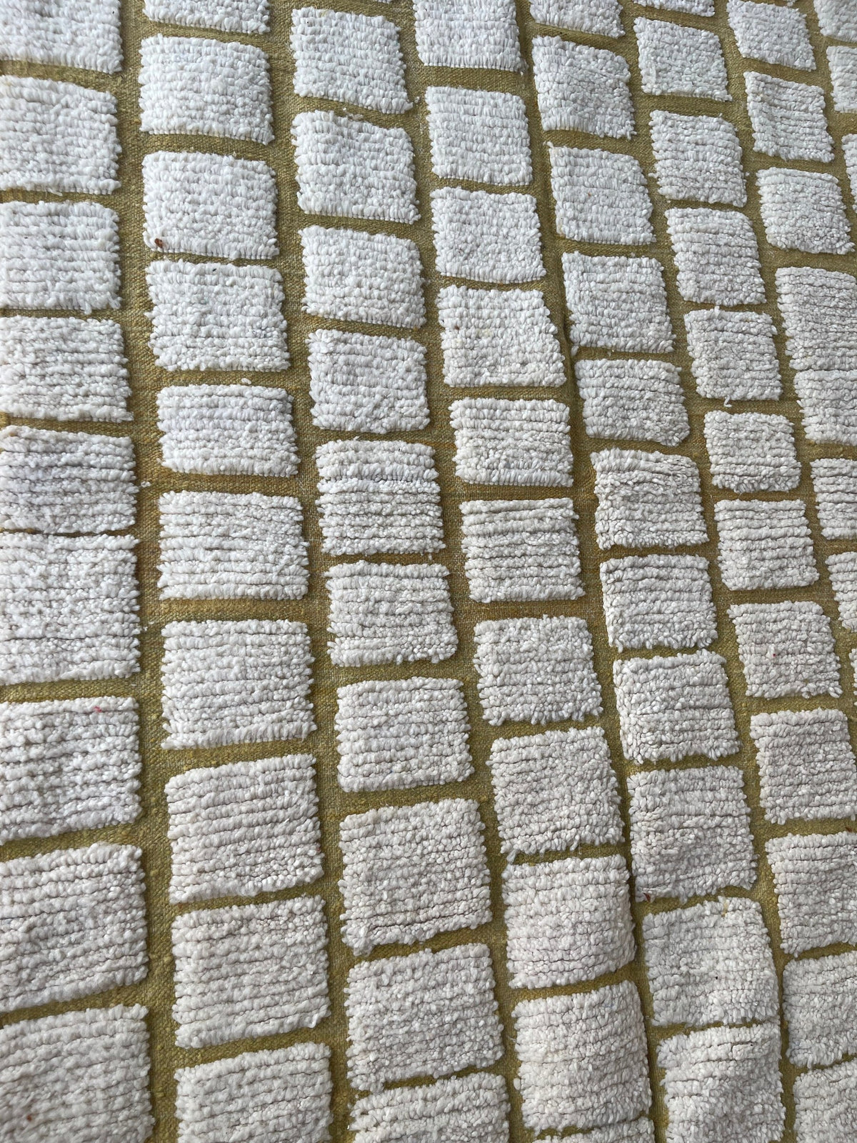 Gros plan sur la laine du tapis berbère Igoudar, laine de mouton au poil ras, blanche et moutarde