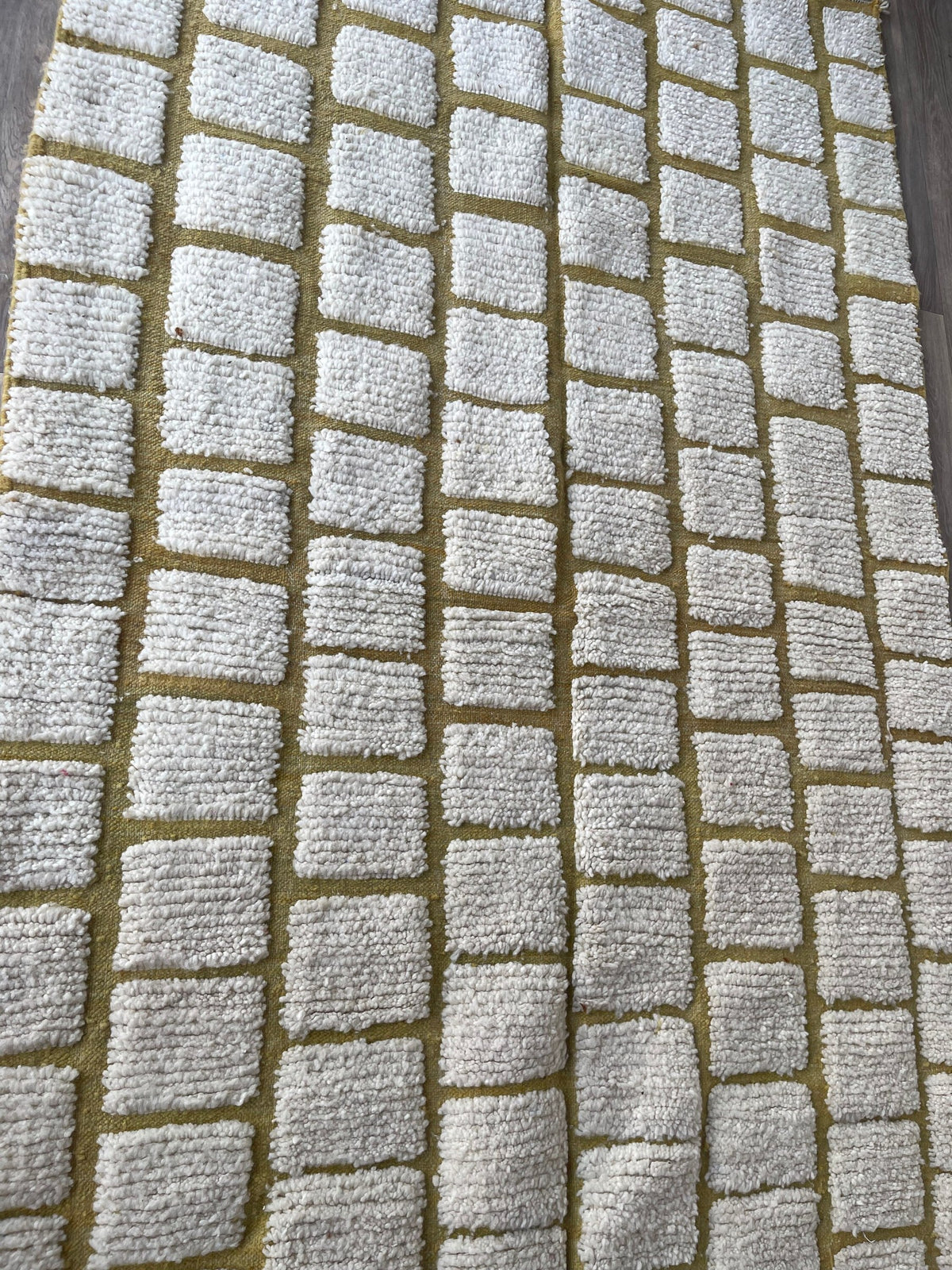 Gros plan sur un détail du tapis berbère Igoudar, poil ras et motif blanc et moutarde vus de près