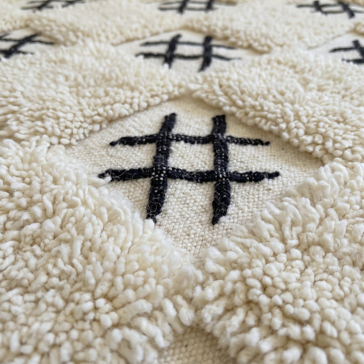 Gros plan sur un motif du tapis berbère Ouaneskra, damier écru d'une dizaine de carrés