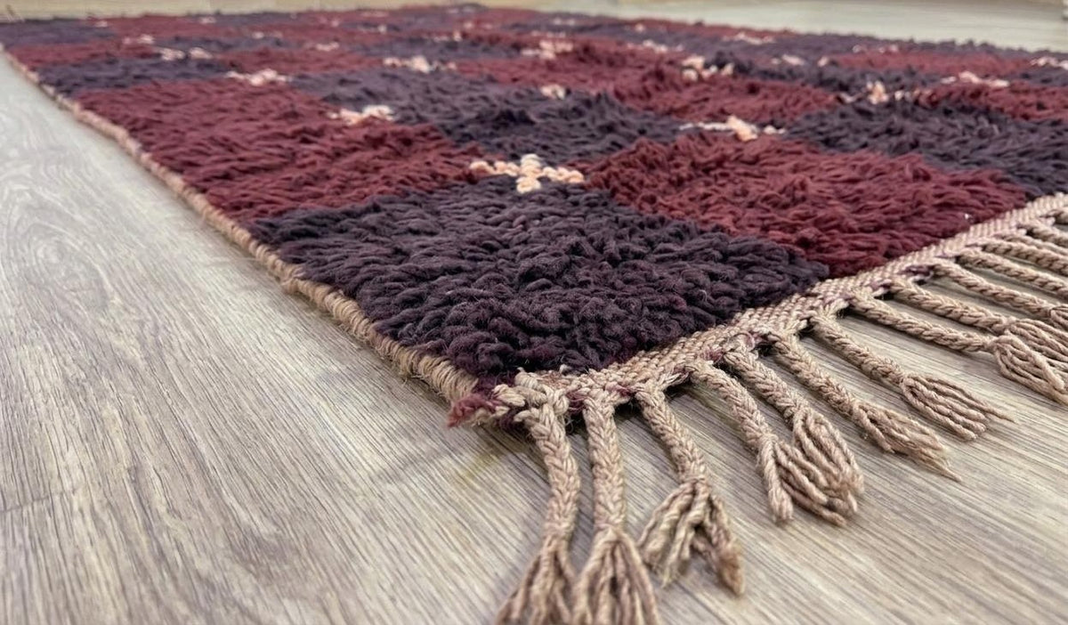 Tapis berbère damier bordeaux et prune Tarwiza posé au sol vu de côté, noué main au Maroc