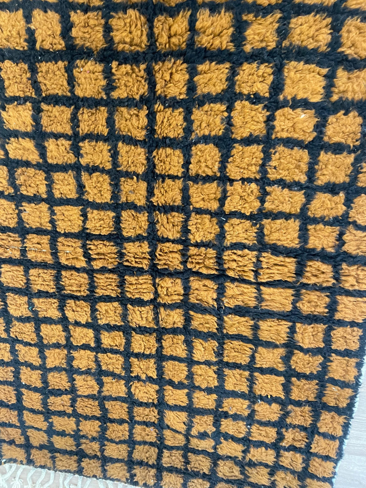 Gros plan sur un détail du tapis berbère Tirgamt, poil long et motif ocre et noir vus de près