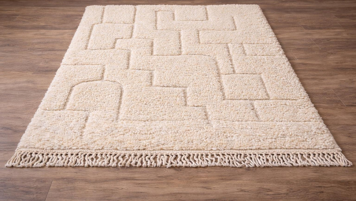 Tapis berbère en relief ivoire Lixus posé au sol vu en biais, noué main au Maroc