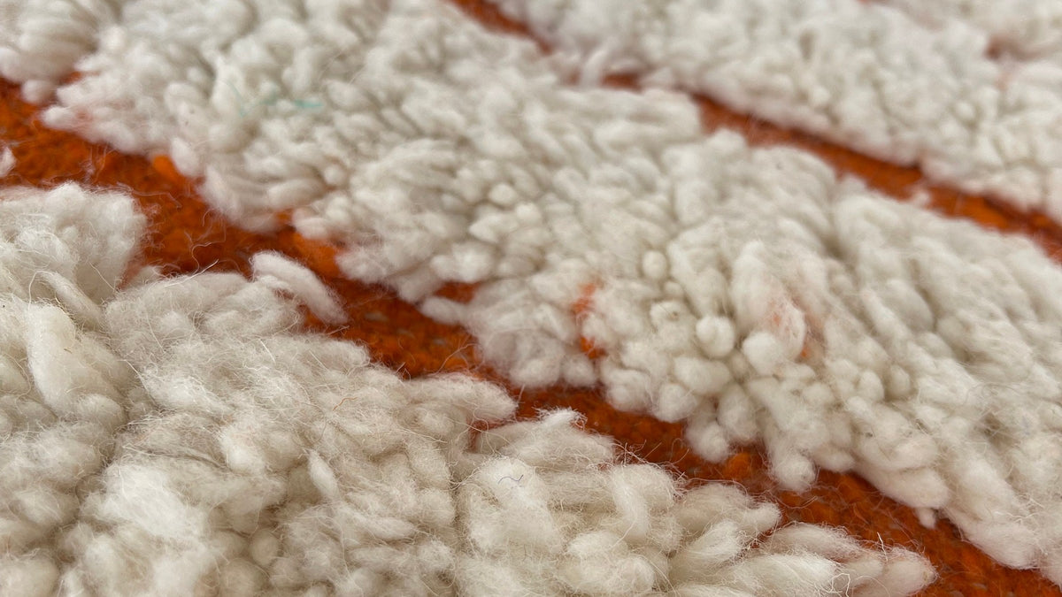 Gros plan sur la laine du tapis berbère Igdat, poil blanc et orange noué à la main