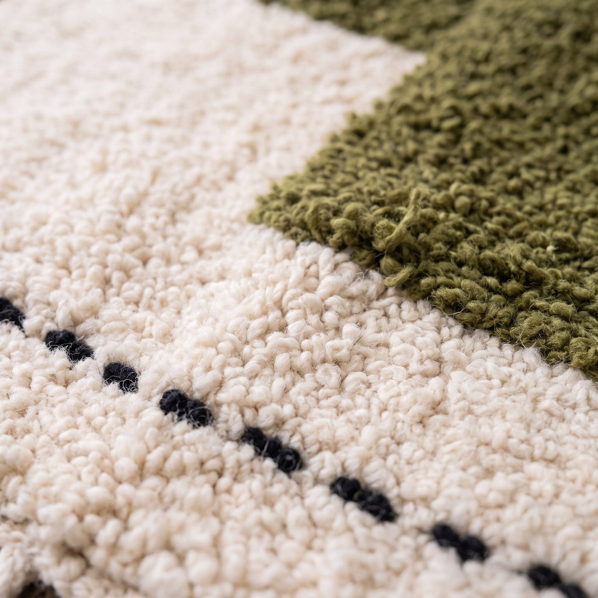 Gros plan sur un motif du tapis berbère Abrid, fond écru bouclé, trois carrés vert olive