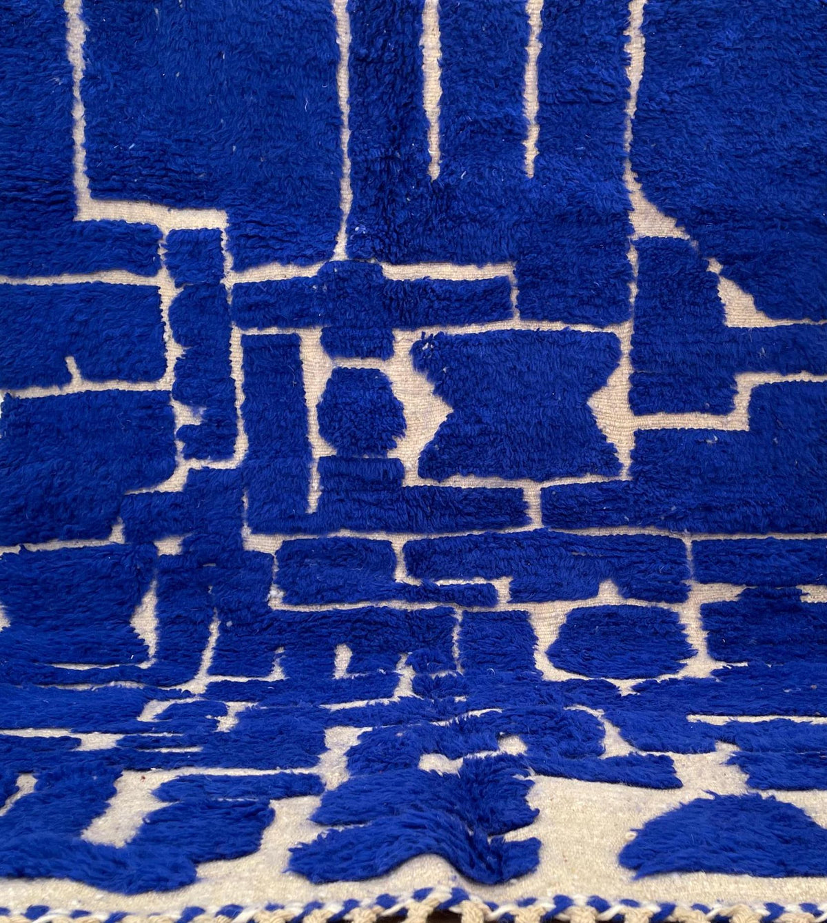 Gros plan sur un détail du tapis berbère Aghmat, poil long et motif bleu roi vus de près