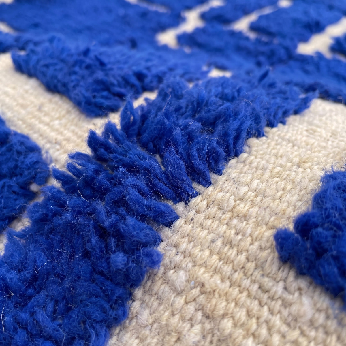 Gros plan sur un motif du tapis berbère Aghmat, fond écru presque couvert de blocs bleu roi