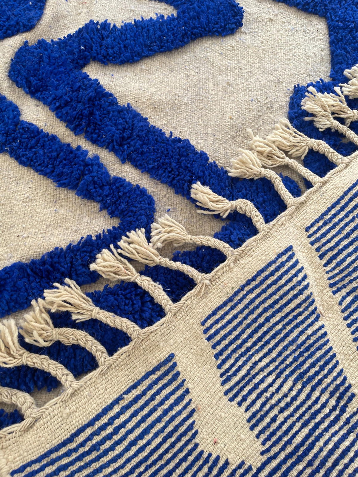 Gros plan sur les franges du tapis berbère Loukkos, écrues tressées à pompons, nouées à la main